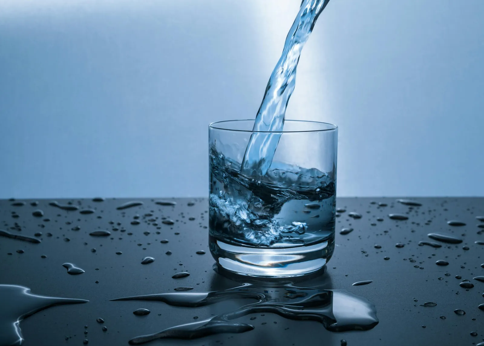 Water pouring into a glass on a dark, wet surface.